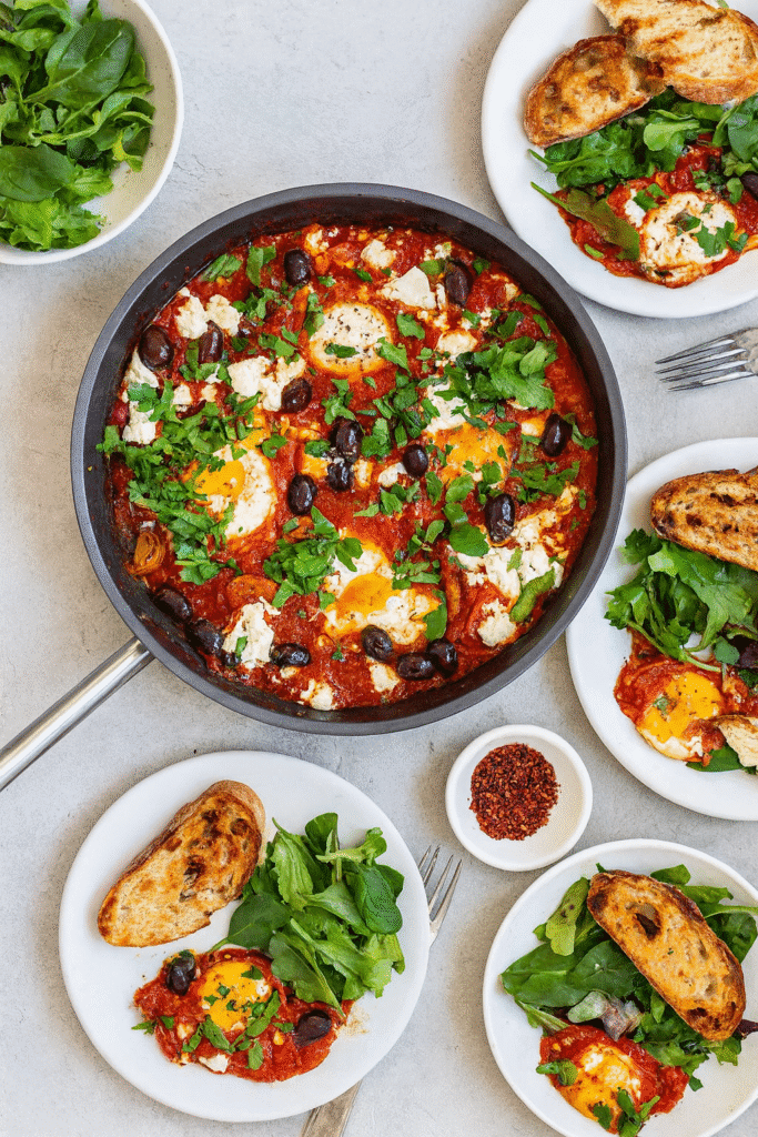 Family style table with shakshuka in a skillet served with bread and salad for a flexible meal.