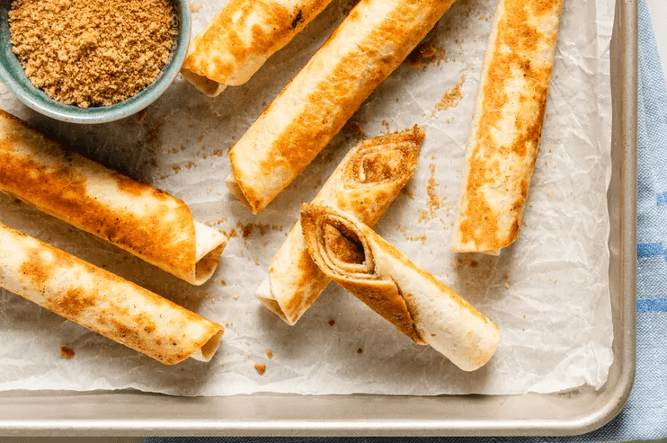 Golden crispy cinnamon-sugar tortilla roll-ups stacked on a tray
