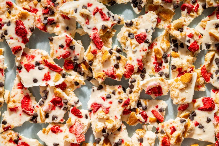 Easy fro-yo bark made with Greek yogurt, strawberries, chocolate chips, and cookie crumbs on a parchment-lined baking sheet