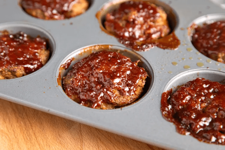 Mini meatloaf muffins baked in a muffin tin with glossy glaze on top and browned edges