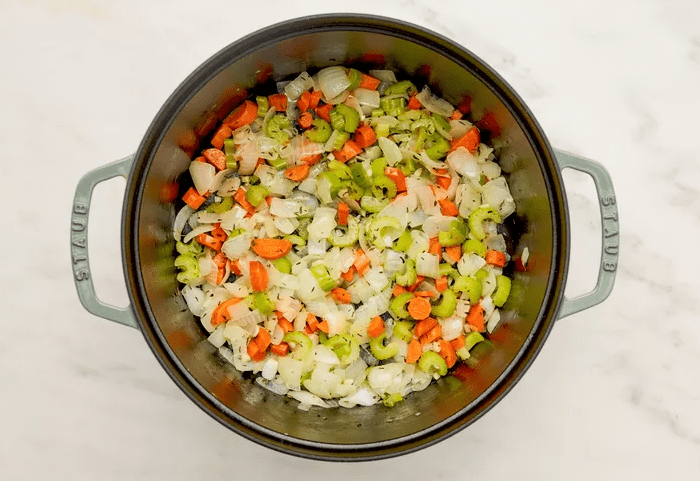 Onion, carrot, celery, and garlic sautéing in butter and thyme in a Dutch oven for chicken pot pie soup