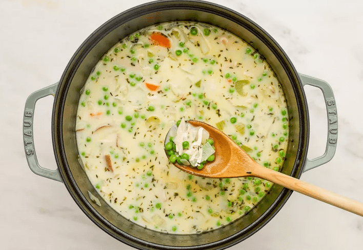 Chicken broth poured over shredded rotisserie chicken and diced potatoes in a pot of chicken pot pie soup
