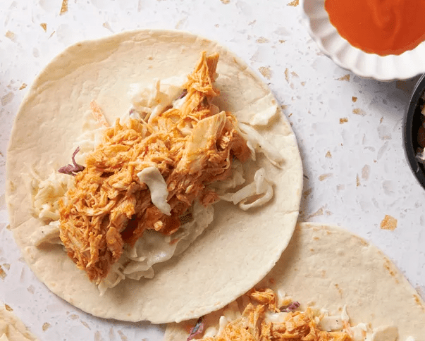 Soft flour tortilla topped with creamy coleslaw and a generous strip of shredded Buffalo chicken, ready to be folded into a taco.