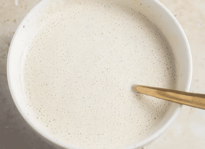 Bowl of creamy halal cart–style white sauce with a spoon after whisking until smooth.