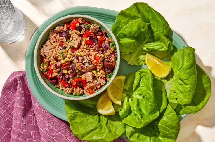 Italian tuna salad with olive oil roasted red peppers olives and herbs in a white bowl with lemon