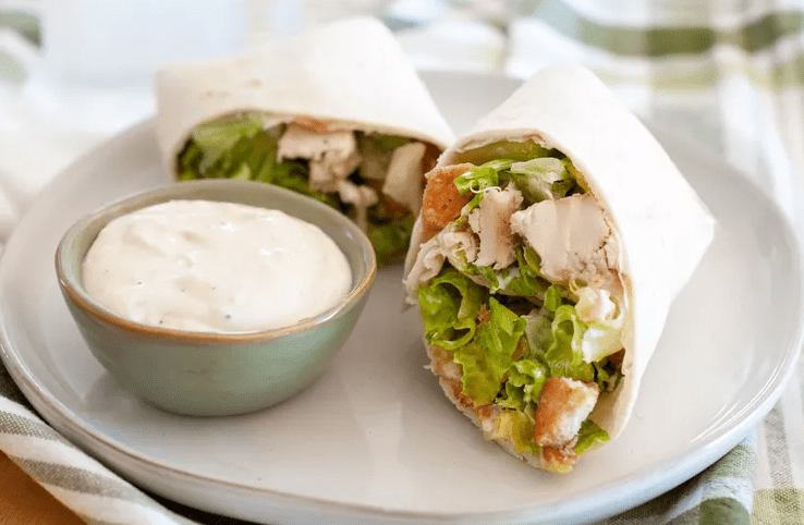 Chicken Caesar wraps cut in half on a plate with the white sauce