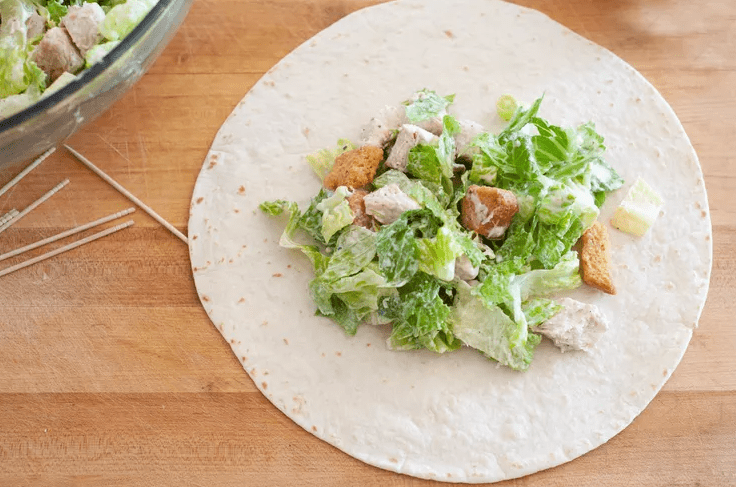 Warm flour tortilla with chicken Caesar filling arranged in the center ready to roll.