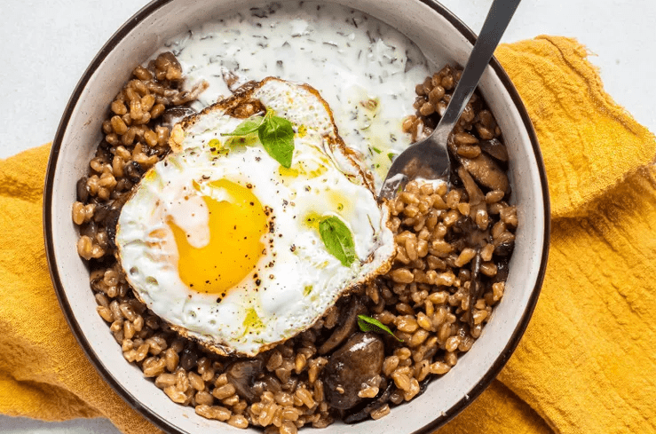 Close up of farro grains with mushrooms, fried egg, and herb yogurt showing chewy and creamy textures.