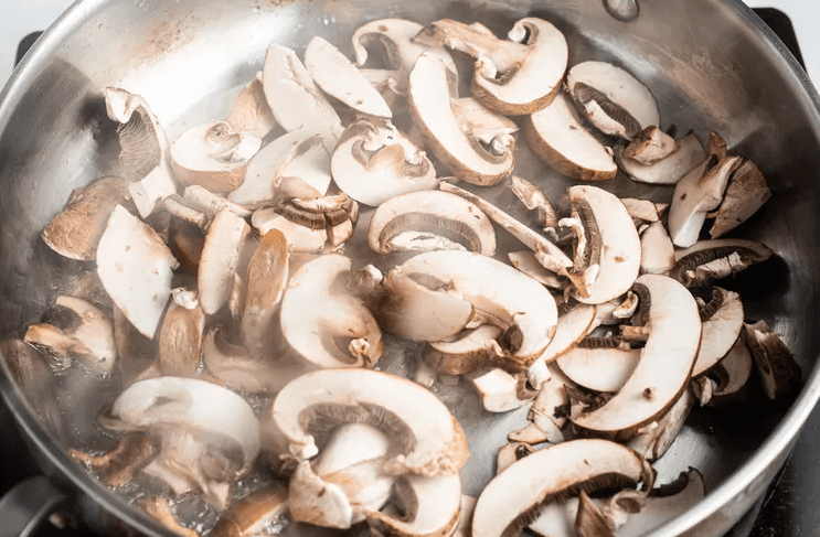 Cremini mushrooms searing in a wide skillet in a single layer for farro mushroom grain bowls.