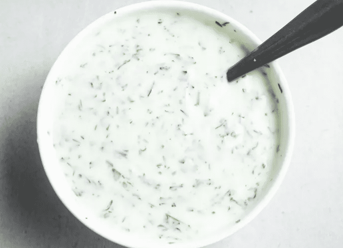 Greek yogurt mixed with fresh herbs and garlic in a small bowl for topping farro mushroom and egg grain bowls.