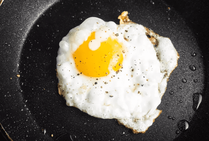 Eggs frying in a nonstick skillet with set whites and runny yolks for topping farro mushroom grain bowls.