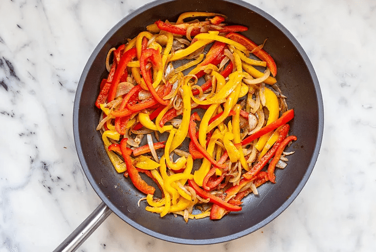 Onions and red and yellow peppers softening in a skillet with cumin and smoked paprika.