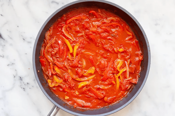 Crushed whole canned tomatoes poured into a skillet of sautéed peppers to build the shakshuka sauce.