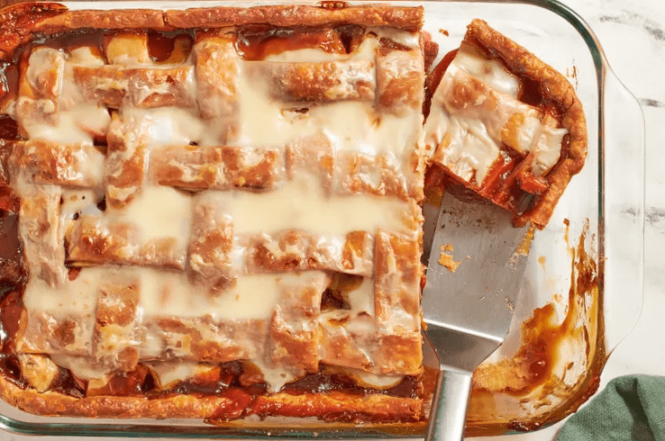 Partially eaten sweet potato sonker in a glass baking dish with a serving spoon and crumbs on the table