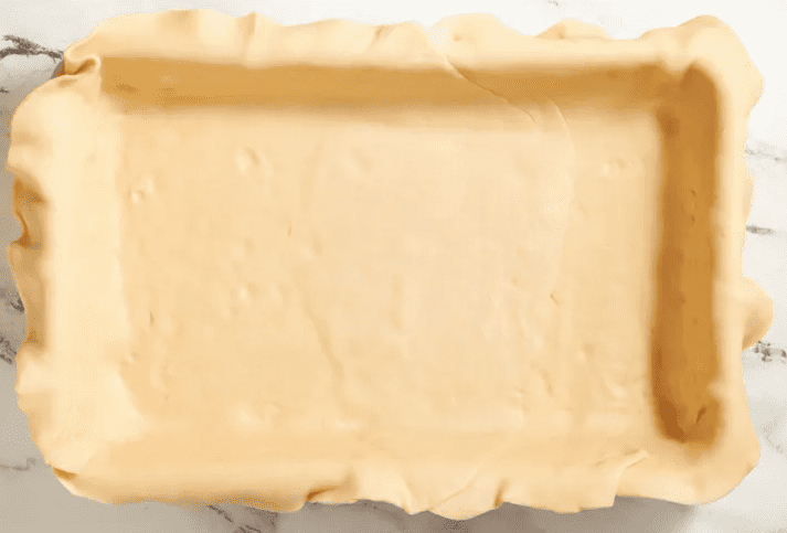 Glass baking dish lined with pie crust pressed up the sides with a rolling pin and dough trimmings beside it