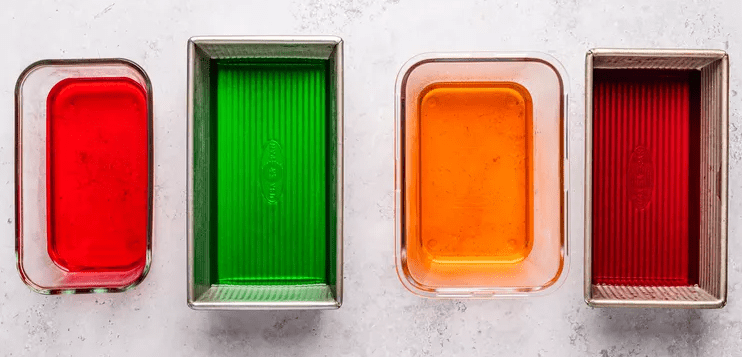 Shallow containers filled with red green yellow and orange liquid gelatin ready to chill