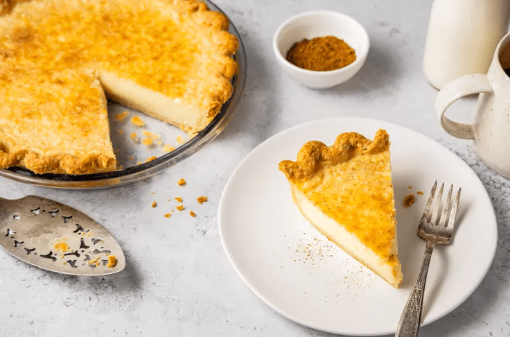 Classic Southern egg custard pie with a slice on a plate and nutmeg on top