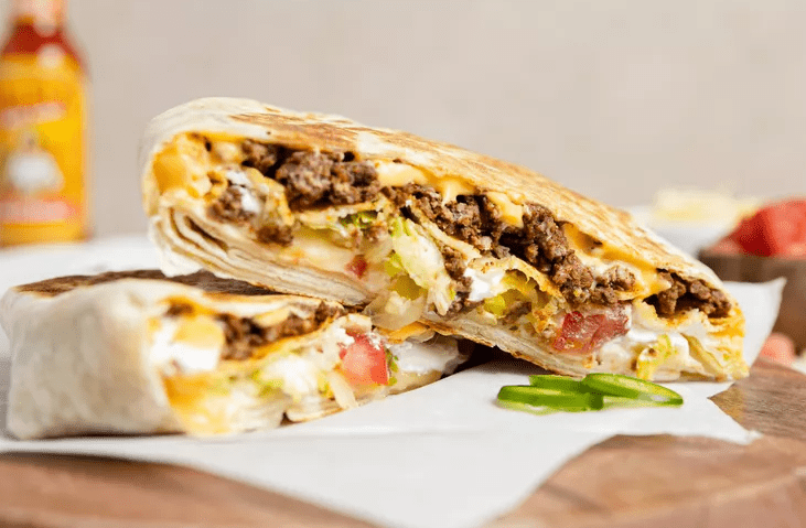 Close-up of a homemade Crunchwrap Supreme showing layers of taco beef, tostada shell, nacho cheese, lettuce, and tomato