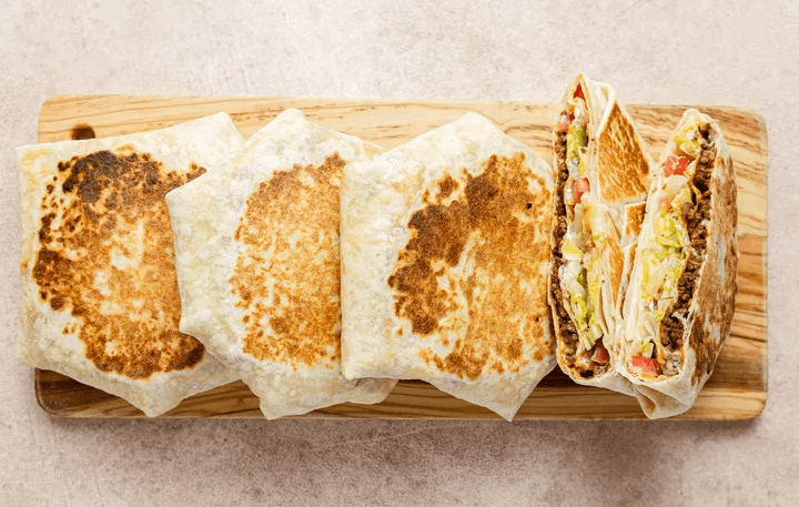 Griddled Copycat Crunchwrap Supremes on a wooden board with one cut open to show the layers