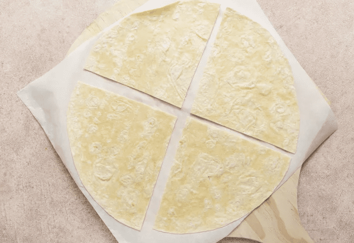Large flour tortilla cut into four wedges on parchment paper for assembling a Copycat Crunchwrap Supreme