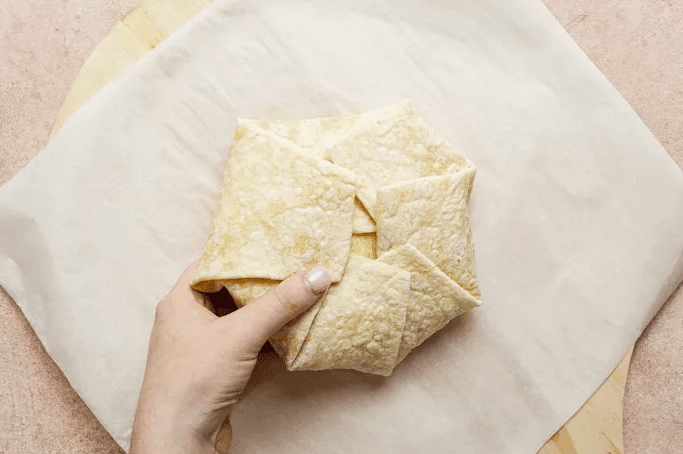 Hand folding a flour tortilla to make a homemade Copycat Crunchwrap Supreme