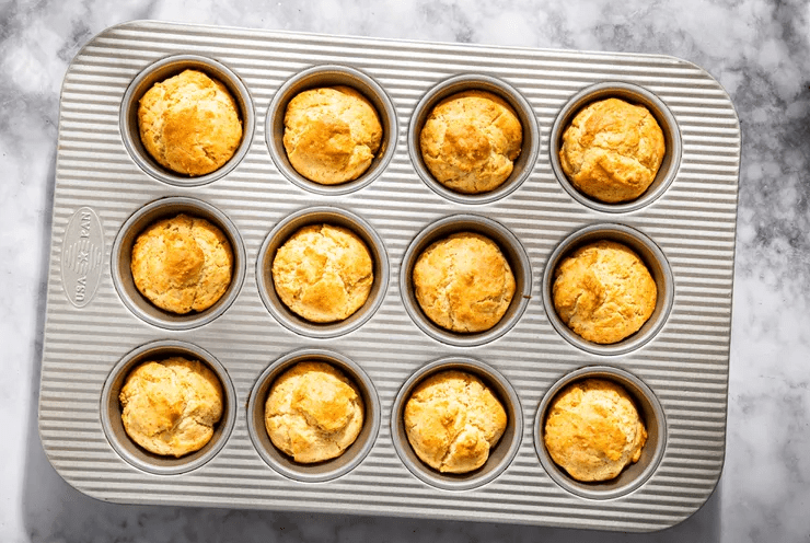 Golden 3-ingredient muffins baked in a 12-cup muffin pan on a marble countertop.