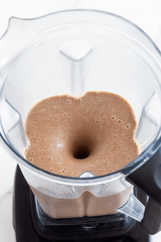 Action shot of the blender in motion with a creamy light brown smoothi