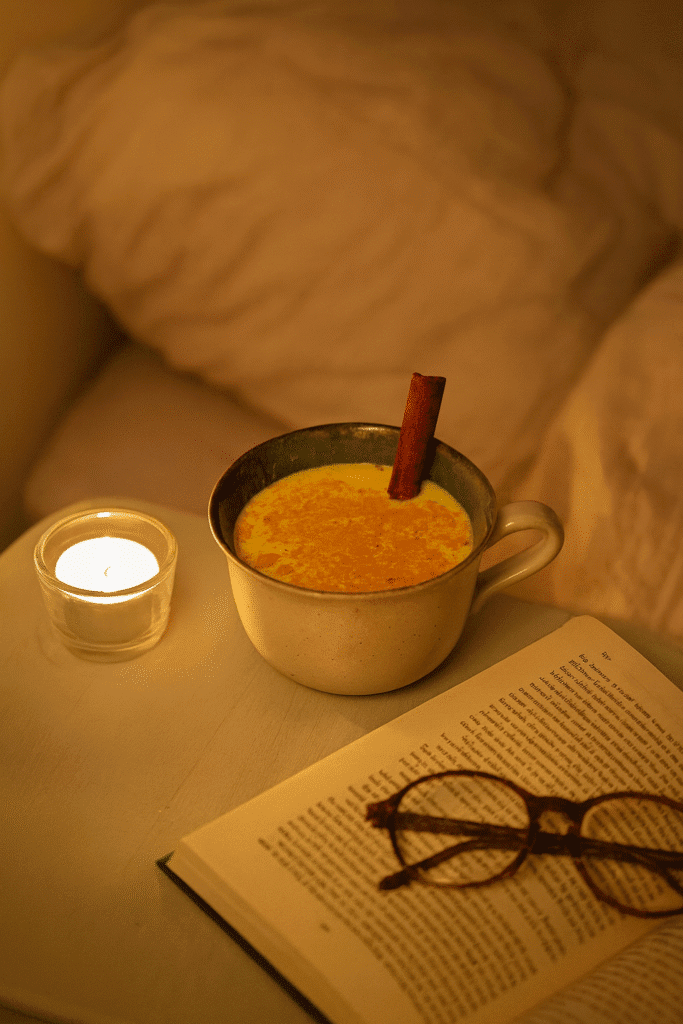 Mug of coconut golden milk on a bedside table with a book and candle