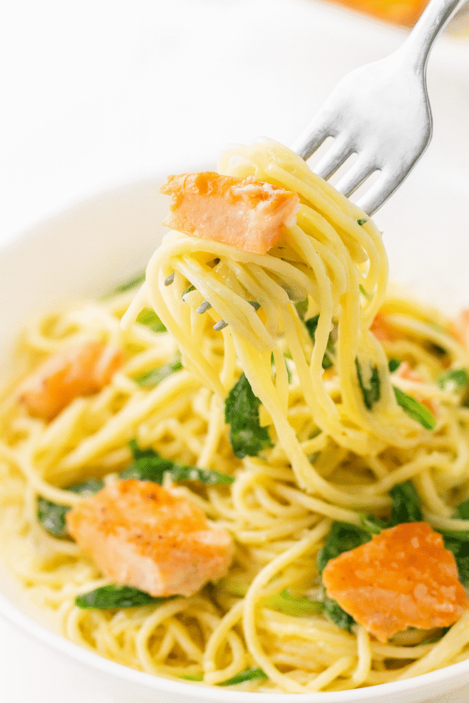Fork twirling creamy angel hair pasta with salmon and arugula in a lemon Parmesan sauce, showing the silky texture and rich flavor.