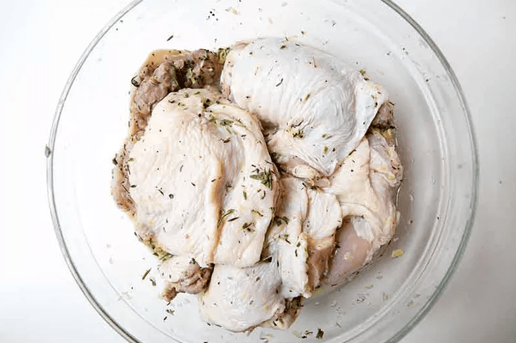Chicken pieces coated in lemon herb marinade in a large bowl