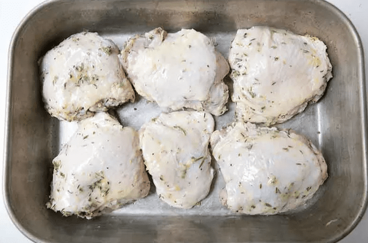 Marinated lemon chicken pieces arranged skin side up in a baking dish with lemon slices