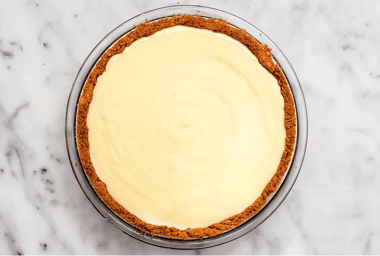 Creamy lemon filling being poured into a graham cracker crust set on a baking sheet