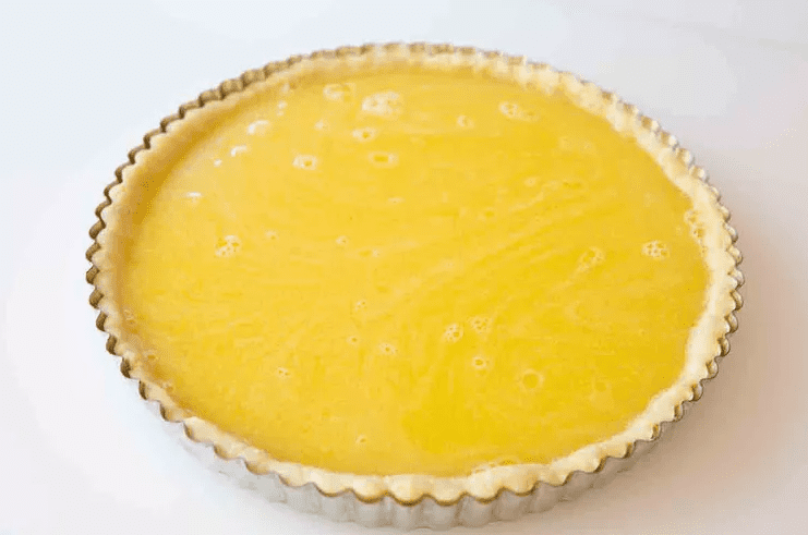Pouring lemon filling into a blind baked tart crust before baking