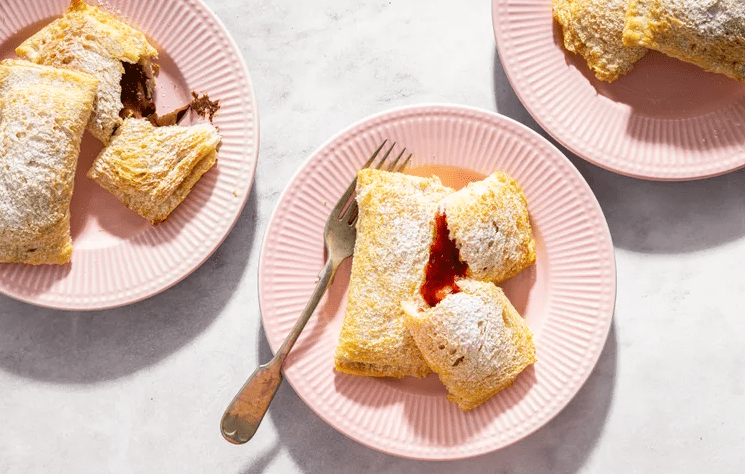 Toast pies on a plate dusted with powdered sugar and one torn open to reveal warm jam inside