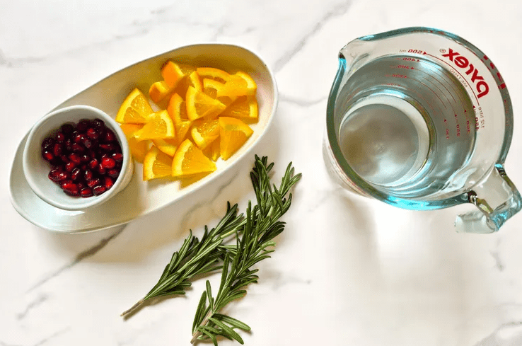 Glass of sparkling drink with colorful fruit and herbs against soft holiday lights.