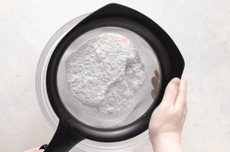 Almond flour and powdered sugar being sifted through a fine mesh sieve for smooth macaron shells.