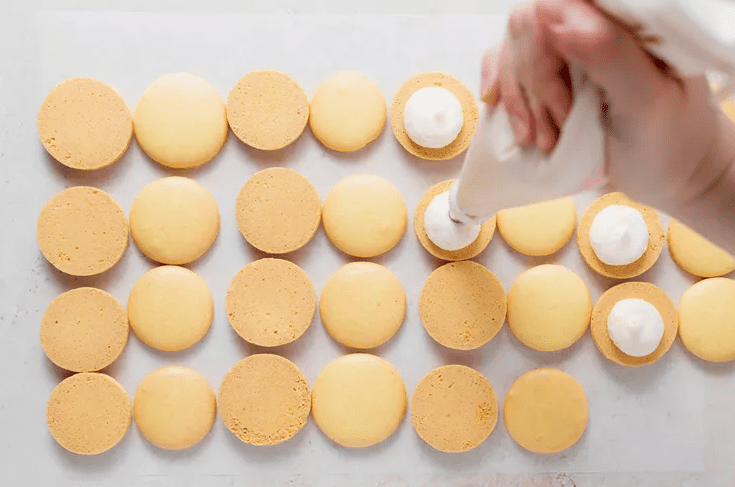 Lemon macaron shells on a baking tray with risen tops and ruffled macaron feet after baking.