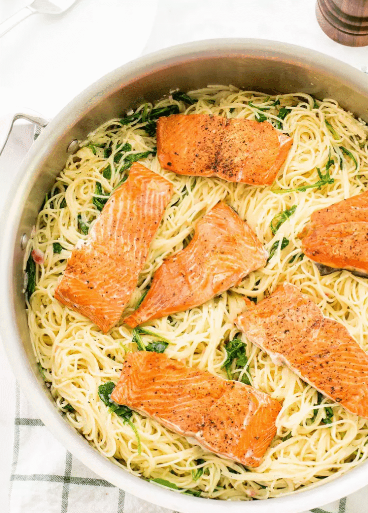 Angel hair pasta with seared salmon, arugula, and creamy lemon Parmesan sauce served in a bowl