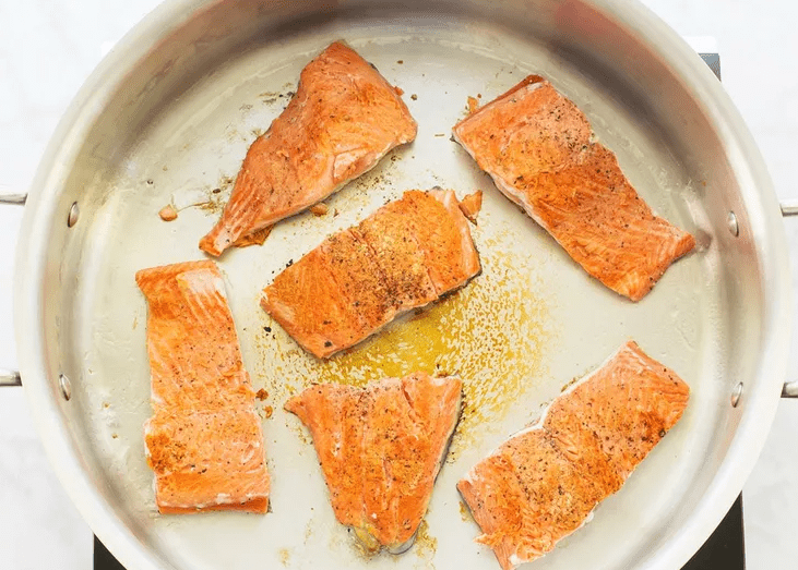 Salmon fillets searing in a hot skillet until golden brown for creamy lemon Parmesan angel hair pasta.