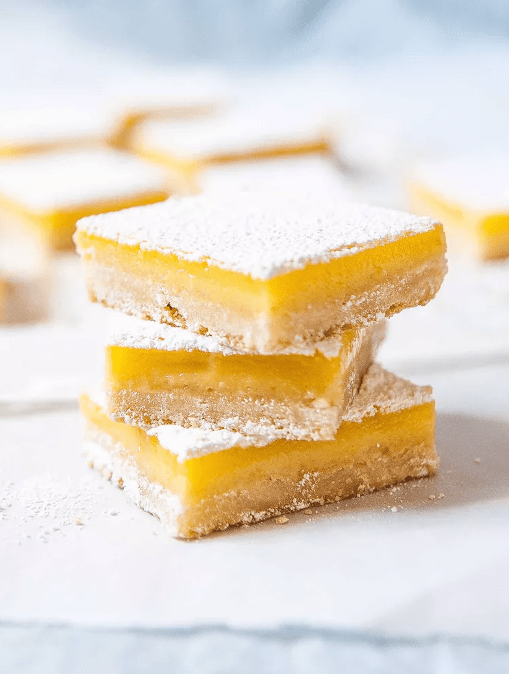 Classic lemon bars with powdered sugar on shortbread crust arranged on parchment 
