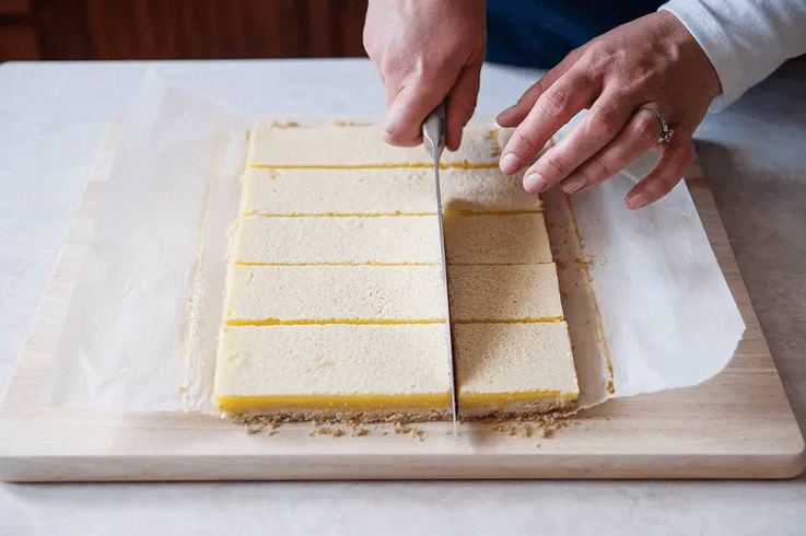 Cutting chilled classic lemon bars into neat squares with a long sharp knife