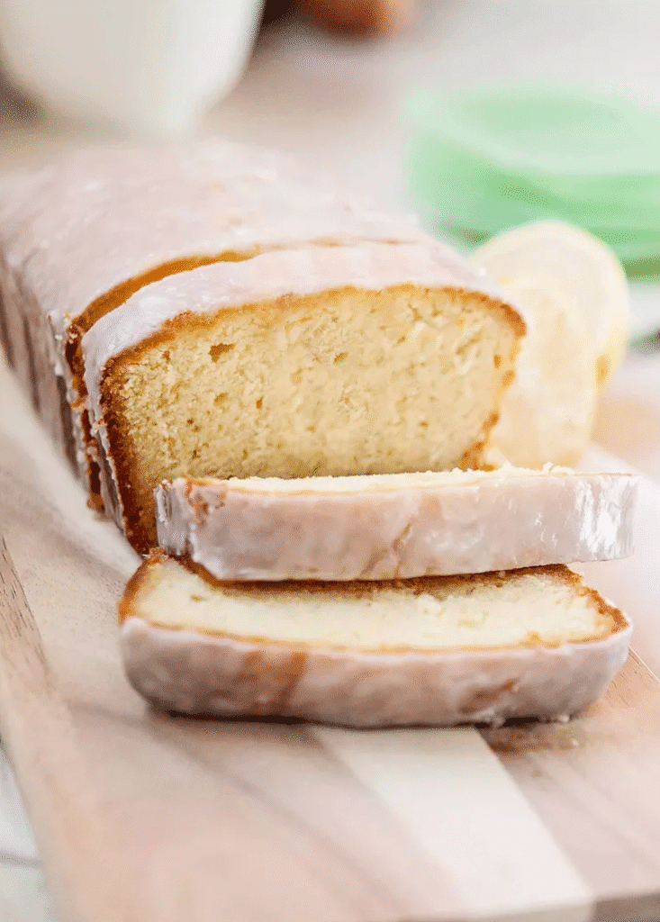 Freshly glazed lemon pound cake loaf on a chopping board with sliced pieces and lemon 