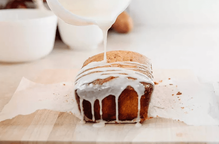 Thick lemon glaze being poured over a cooled lemon pound cake loaf so it slowly drips down the sides