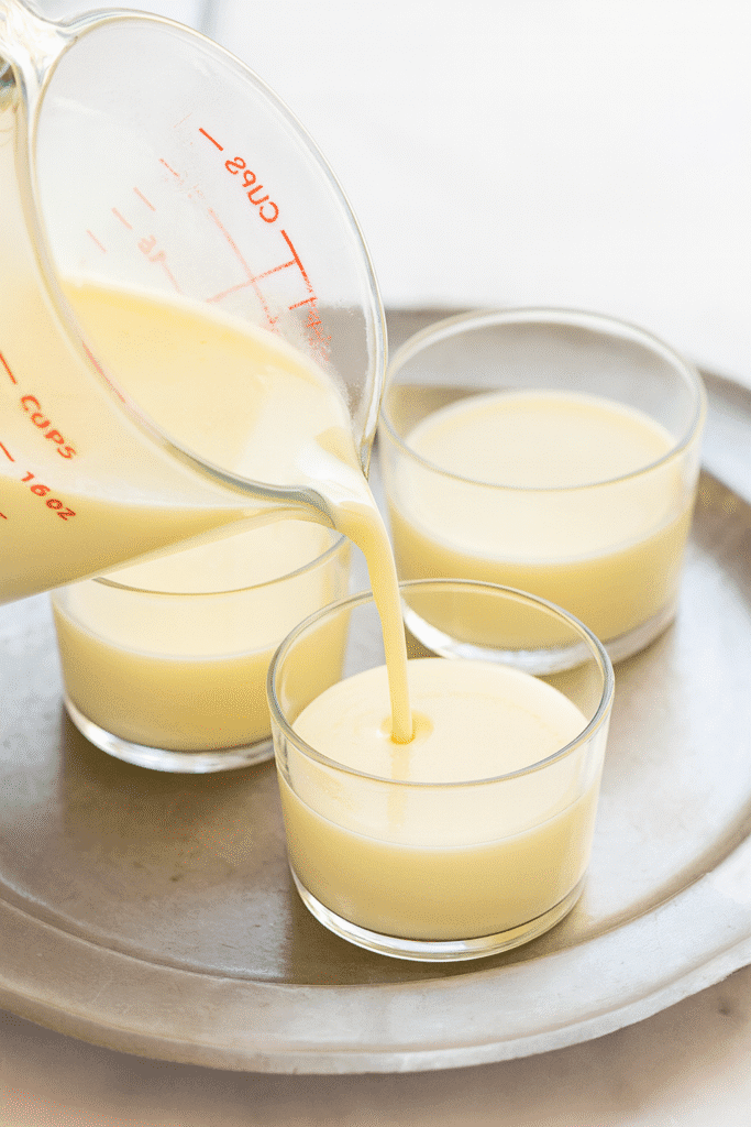 Strained lemon pudding mixture poured into small glass dessert cups on a tray