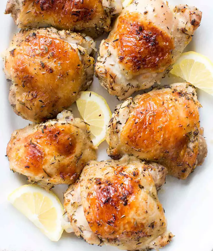 Golden roasted lemon chicken thighs on a white platter with crispy skin and lemon wedges