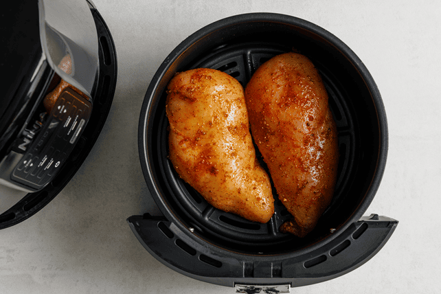 Seasoned chicken breasts in the air fryer basket
